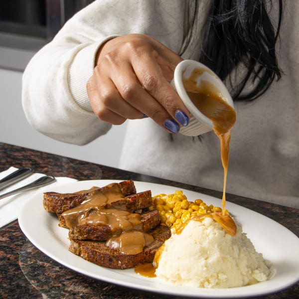 A hand pours gravy over meatloaf, mashed potatoes, and corn on a white plate at Seaport Diner.