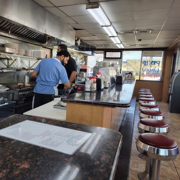 Two chefs cooking behind a long counter with red-seated bar stools at Seaport Diner.