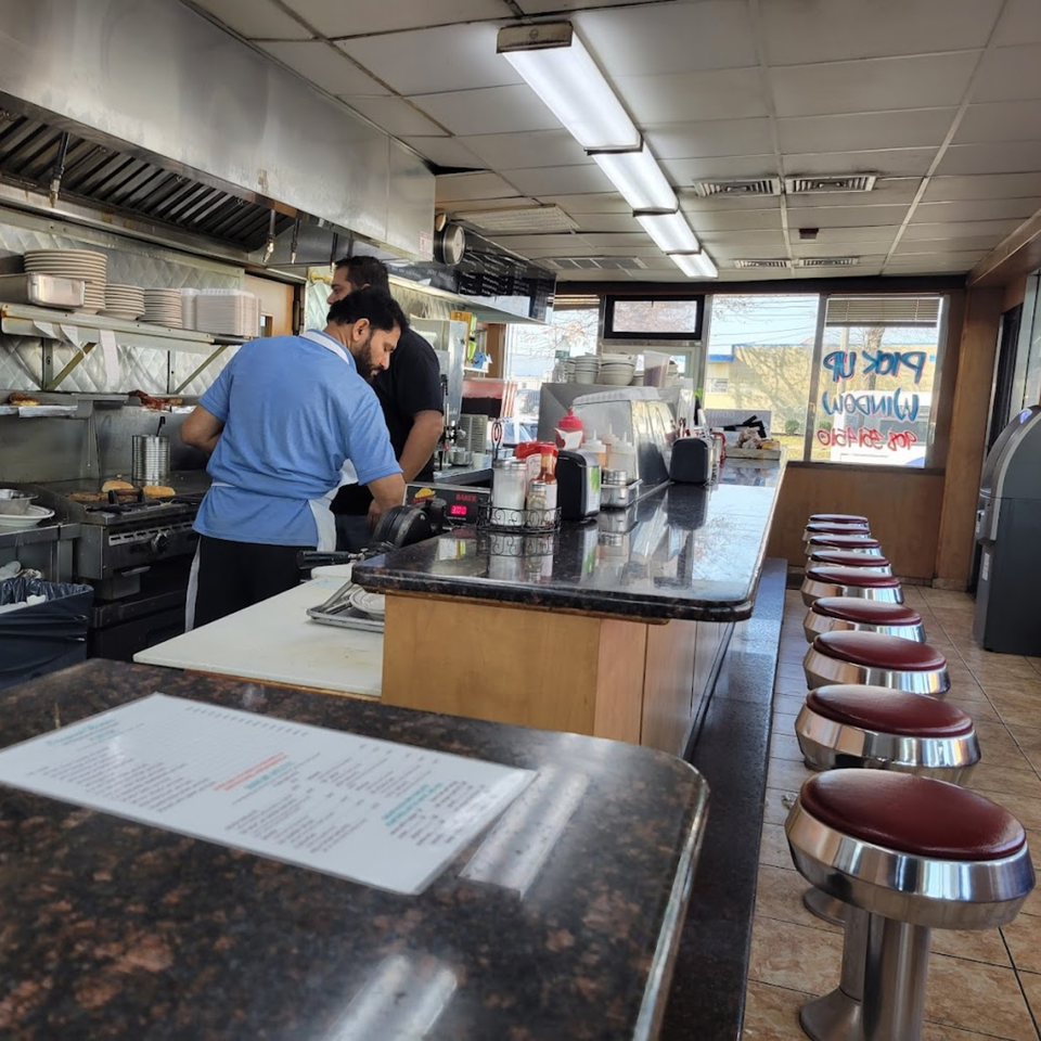 Two chefs cooking behind a long counter with red-seated bar stools at Seaport Diner.