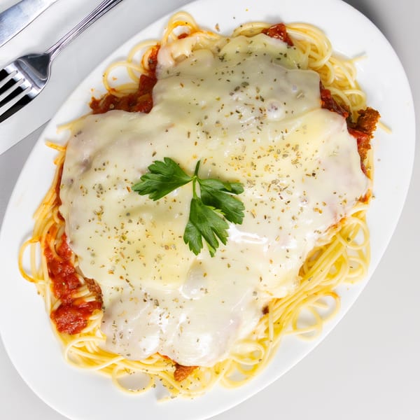 Chicken Parmesan with spaghetti, red sauce, melted cheese, and parsley on a white plate.