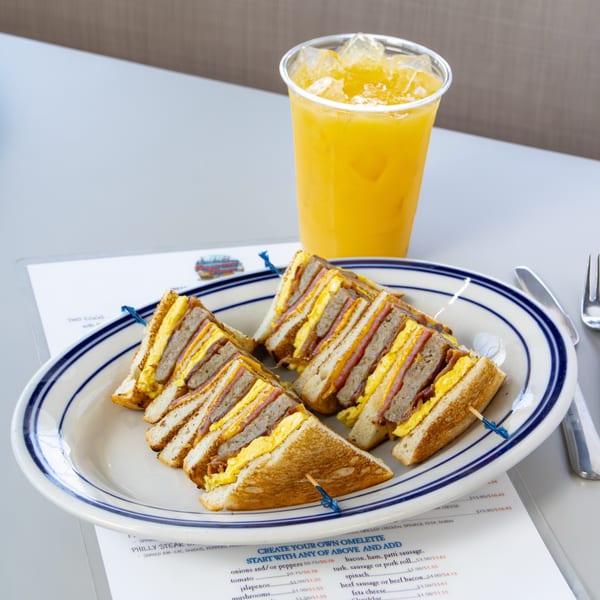 A Seaport Diner breakfast club sandwich with egg, ham, and cheese, served with orange juice.