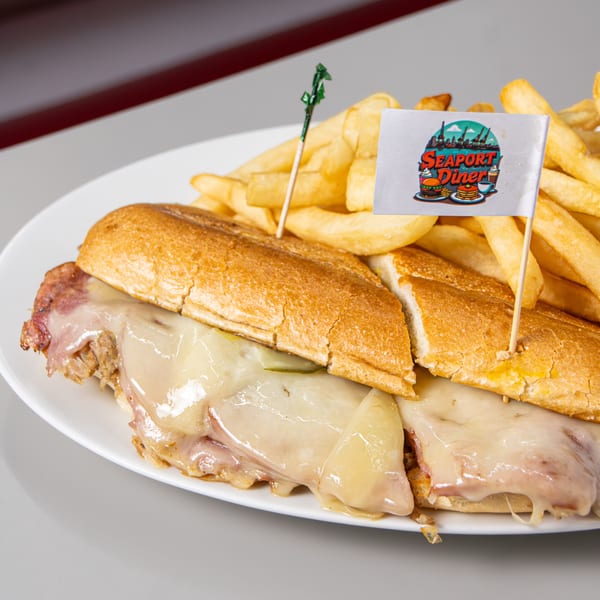 A Seaport Diner cheesesteak sandwich with melted cheese and fries, adorned with a branded flag.